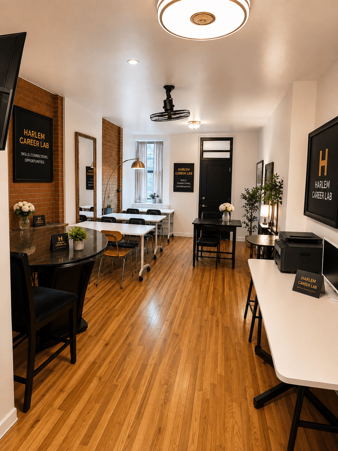 Modern Harlem Career Lab workspace featuring hardwood floors, white tables, black chairs, and brick accents.