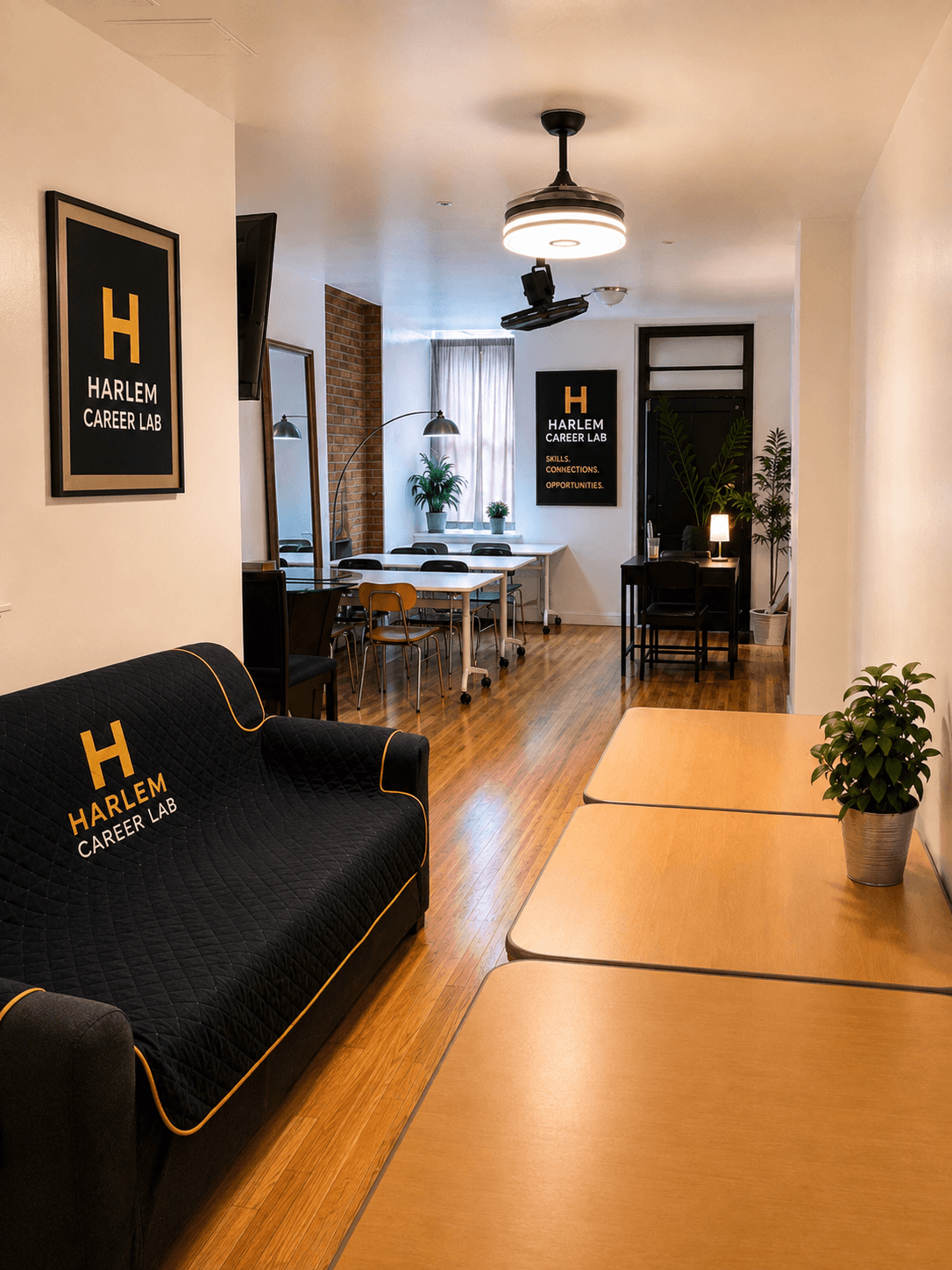 Harlem Career Lab workspace with branded black sofa, wooden floors, and white communal tables.